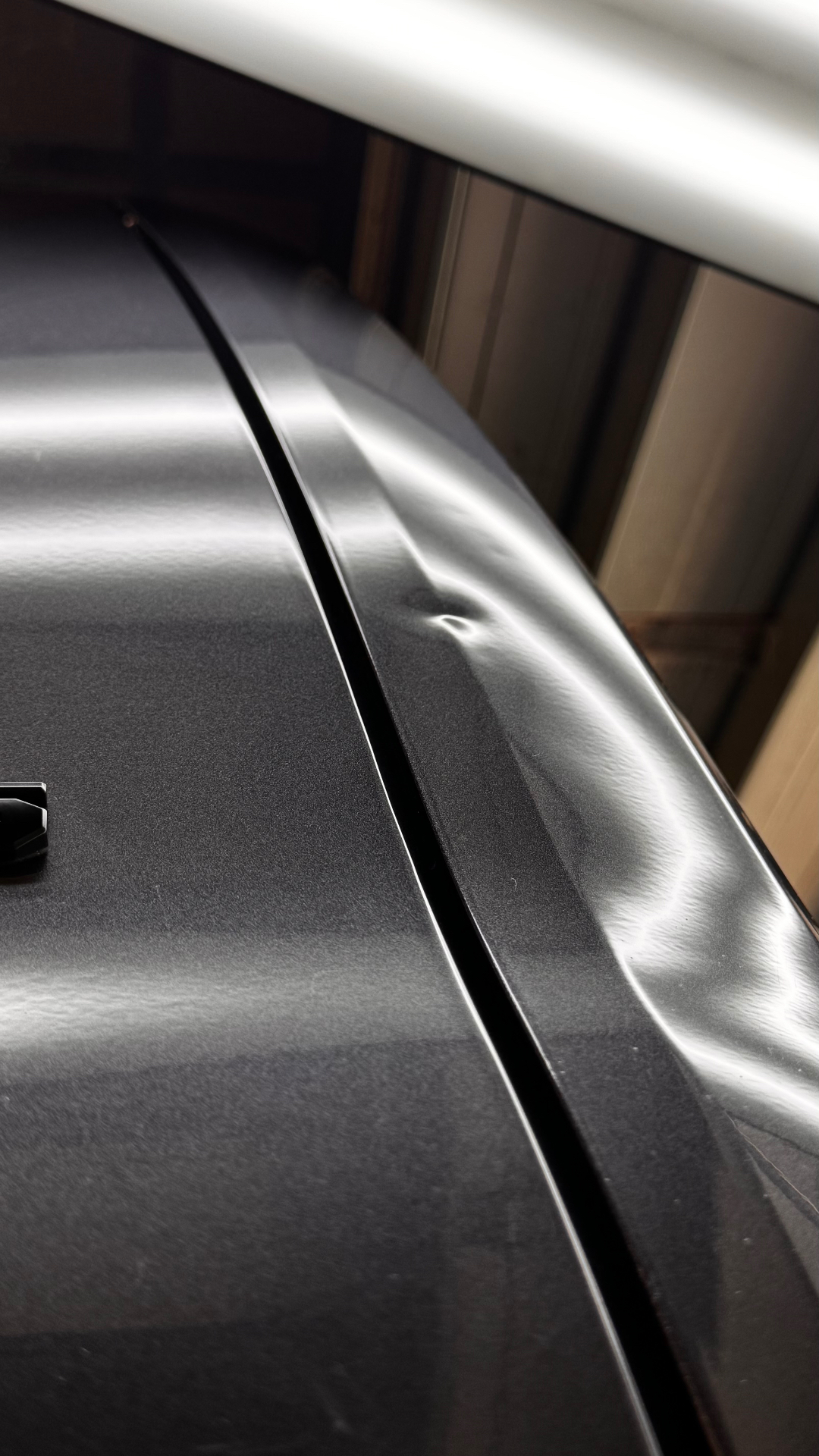 Small dent on a dark vehicle panel under PDR reflection lighting