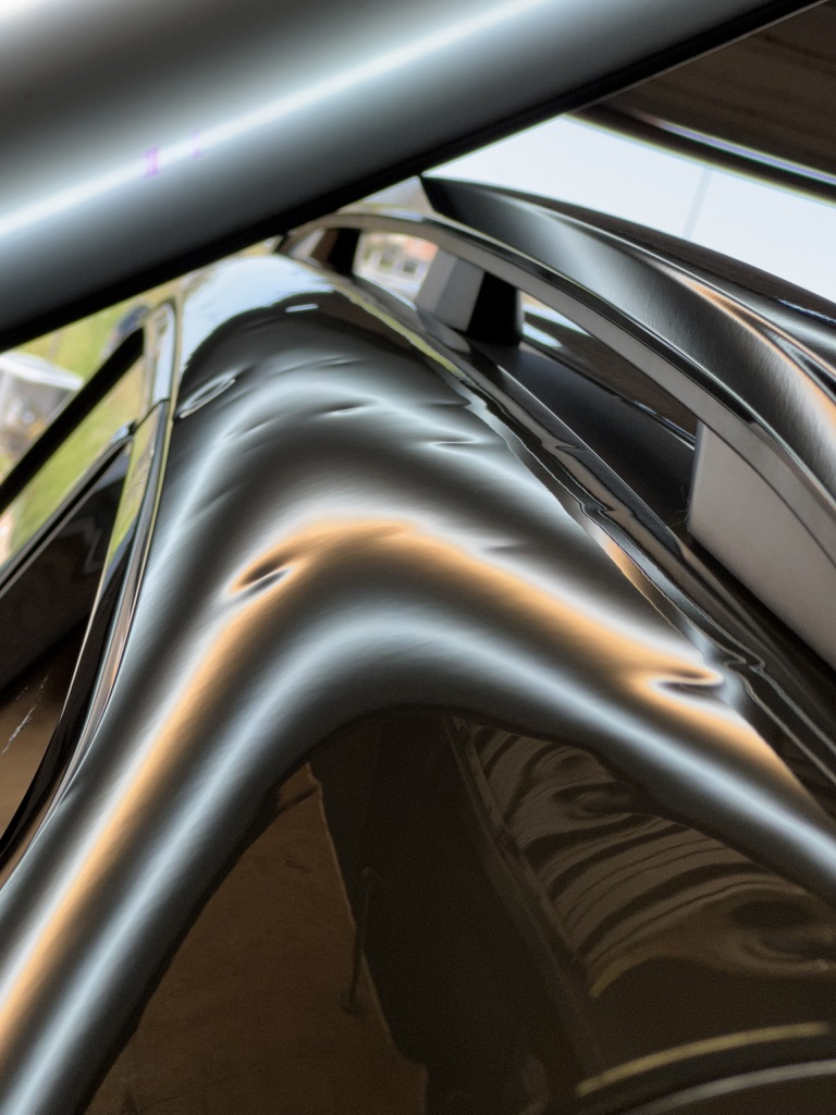 Hail dents across a dark roof rail under reflection lighting