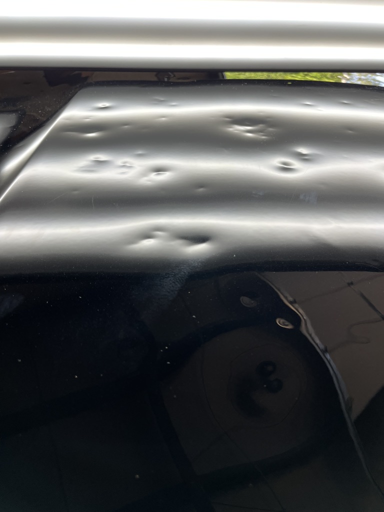 Multiple hail dents highlighted across a dark vehicle roof