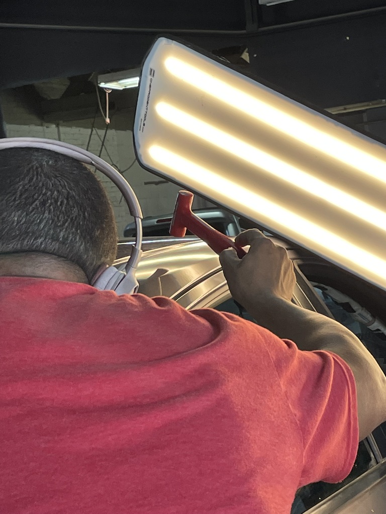 PDR technician tapping a dent beneath a bright reflection light
