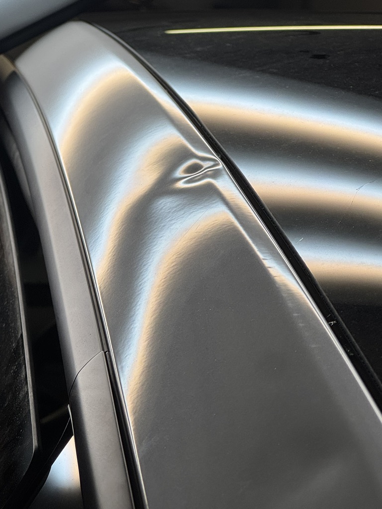 Sharp dent on a silver roof rail revealed by reflection lines